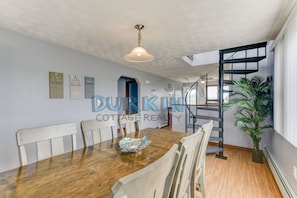A spacious dining area with a wooden table and chairs, a hanging light fixture, and a spiral staircase. - Spacious Colonial, Ocean Views, Close to Beach, Spiral Staircase to Second Floor (Narragansett)