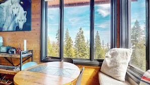A room with a large window, a round wooden table, a chair, and a painting of wolves. - Remodeled Home, Amazing Views, Private Hot Tub & Garage, Near the Lakes Basin (Mammoth Lakes)