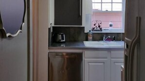 Una cocina compacta con armarios blancos, un lavamanos de acero inoxidable y lavavajillas.
