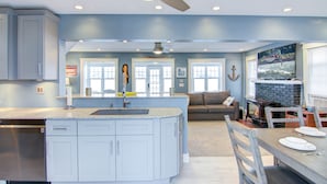 A modern kitchen with a large island, a dining area with a table and chairs, a living room with a sofa, and a fireplace. - Conesus Lake Front Retreat (Conesus)