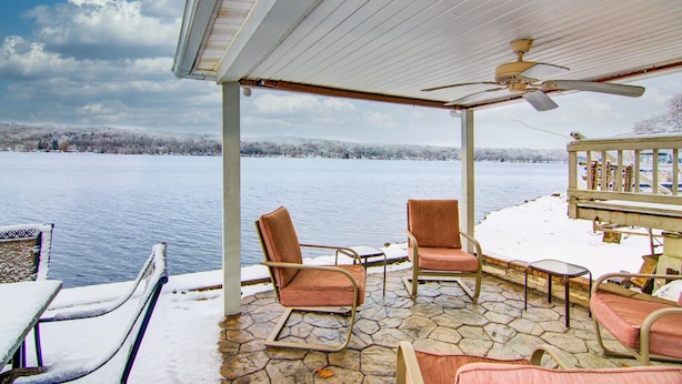 A covered patio with stone flooring, two rocking chairs, a table, and a ceiling fan. - Conesus Lake Front Retreat (Conesus)