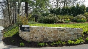 Un mur de pierres avec une boîte aux lettres portant l’inscription « 230 NATHERS » et un chemin pavé à côté.