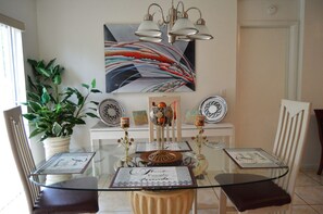 A dining area with a glass table, chairs, a potted plant, a decorative globe, and a wall-mounted painting. - Vacation Stay for Less (Orlando)