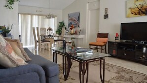 Un salon comprenant un canapé, une table basse en verre, un téléviseur et un coin repas avec des chaises et une table.