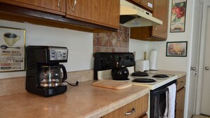 Une cuisine avec des meubles de rangement en bois, une machine à café, une bouilloire et une cuisinière.