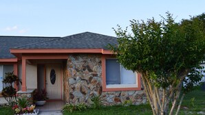 Une maison avec une façade en pierre, un porche à l’avant et un petit arbre dans le jardin.
