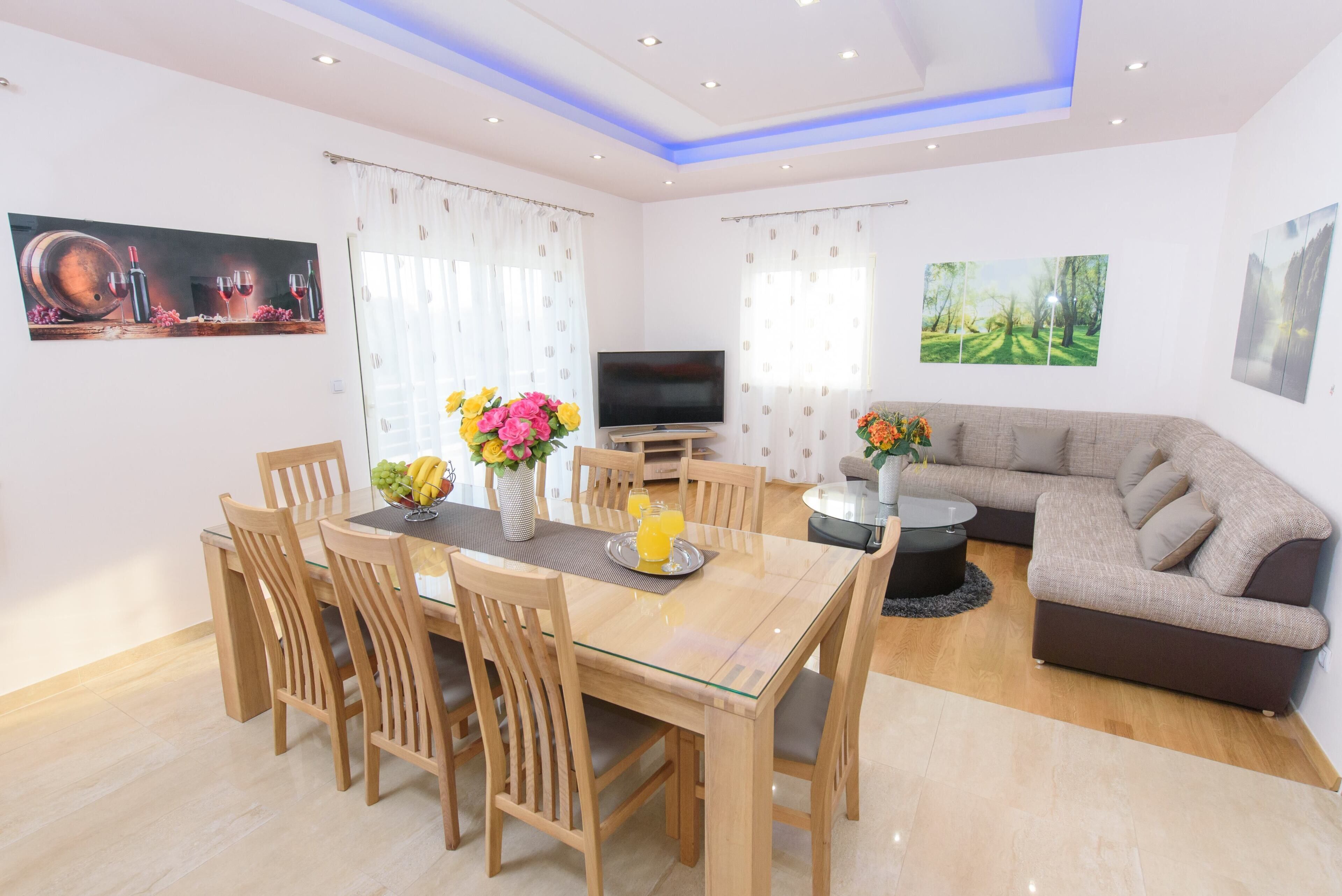 A modern living room with a dining area, a flat-screen TV, and a sofa.