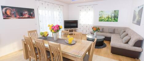 A modern living room with a dining area, a flat-screen TV, and a sofa.