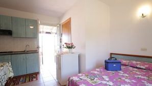 Een compacte kamer met een bed, een kleine keuken en een deur naar een buitenruimte.