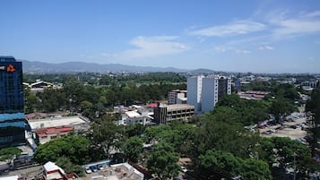 A cityscape with a mix of modern and older buildings, a parking lot, and a view of distant mountains.