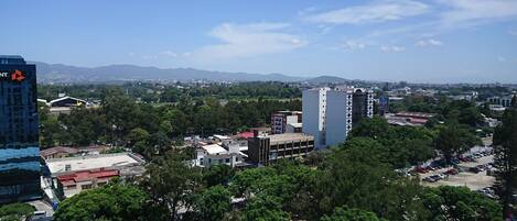 Un paysage urbain mêlant bâtiments modernes et bâtiments plus anciens, un parking et une vue sur des montagnes lointaines.
