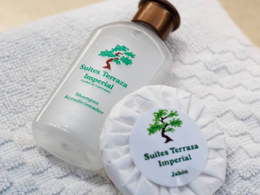 A bottle of shampoo and a round soap bar with a tree logo, both on a white towel.