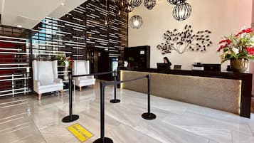 Un área de recepción moderna con un mostrador, dos sillones blancos, una obra de arte decorativa en la pared y una señalización amarilla en el suelo.