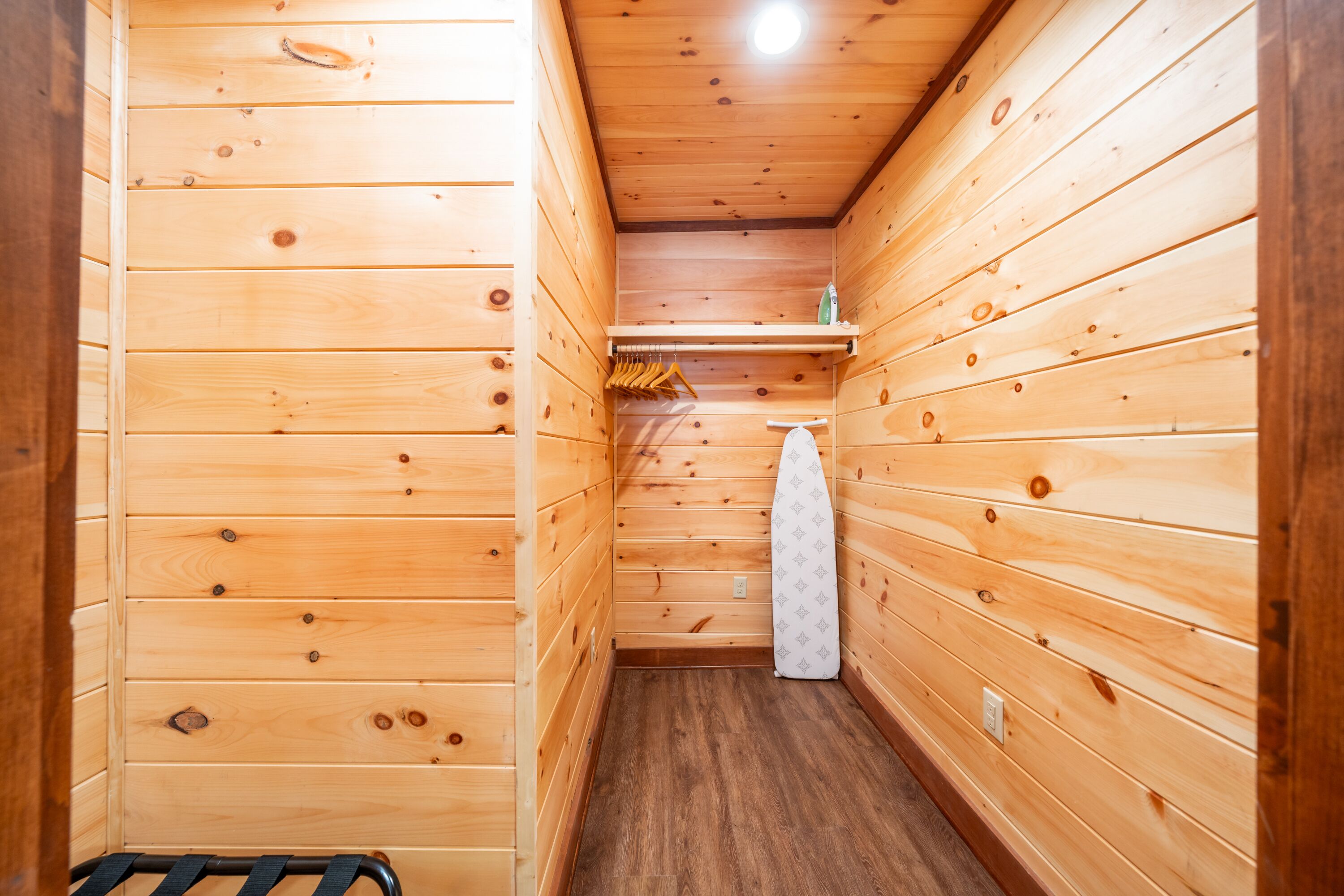 A narrow wooden hallway with a bench on the left, a hanging rack with clothes, and a towel on the right.