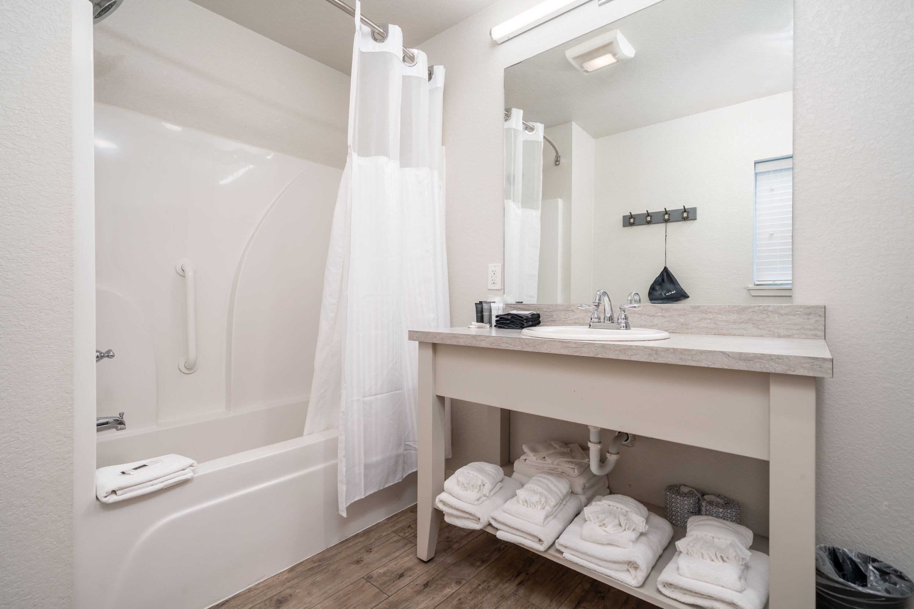 A modern bathroom with a bathtub, a sink, and a mirror. There are towels and toiletries visible.