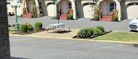 Il s’agit d’un motel composé de plusieurs bâtiments, chacun ayant un toit rouge et des bordures vertes. Un parking se trouve à l’avant, avec une table de pique-nique et des bancs.