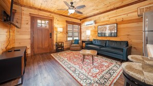 A wooden cabin interior with a ceiling fan, a sofa, a coffee table, a rug, and a refrigerator. - Best  Court (Hot Springs)