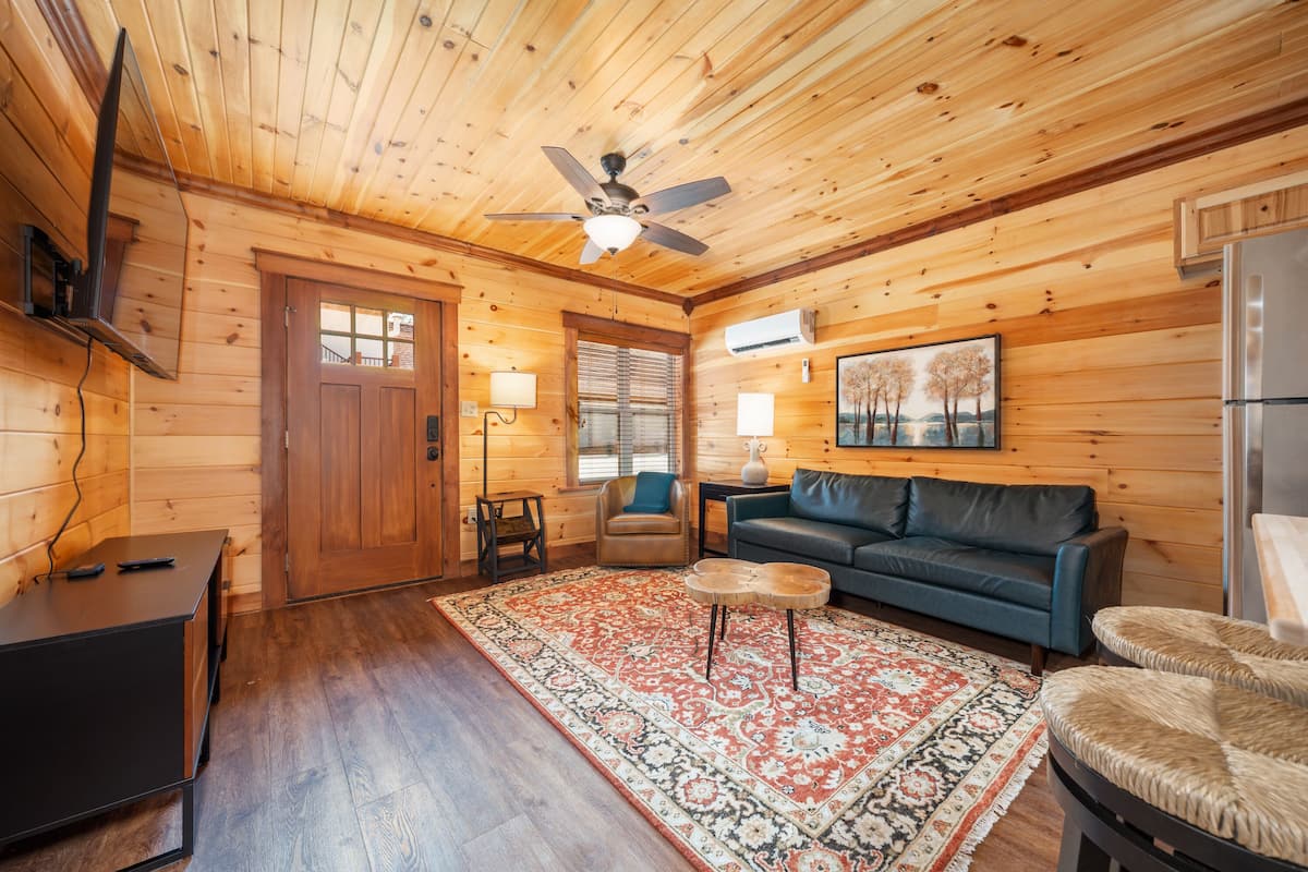 A wooden cabin interior with a ceiling fan, a sofa, a coffee table, a rug, and a refrigerator.