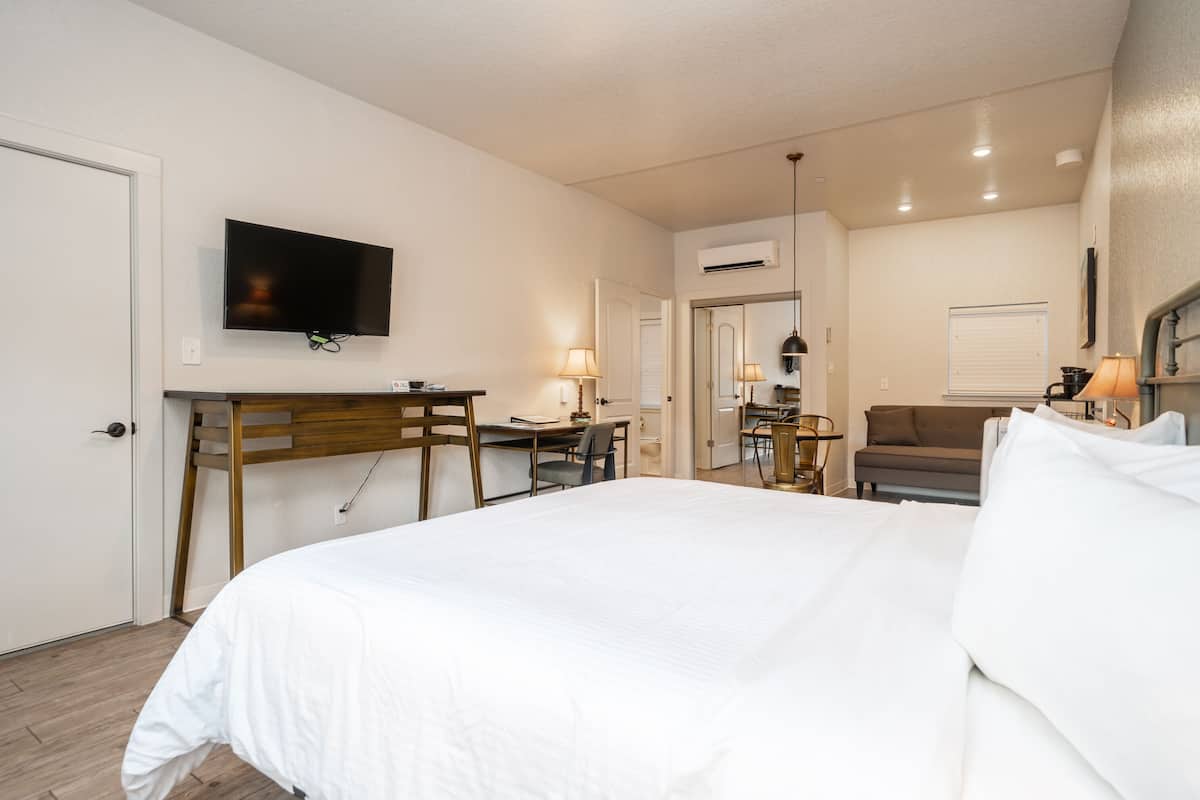 A hotel room with a bed, desk, chair, TV, and a small seating area with a sofa and lamp.
