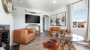 A modern living room with leather sofas, a glass coffee table, a mounted TV, and a fireplace.