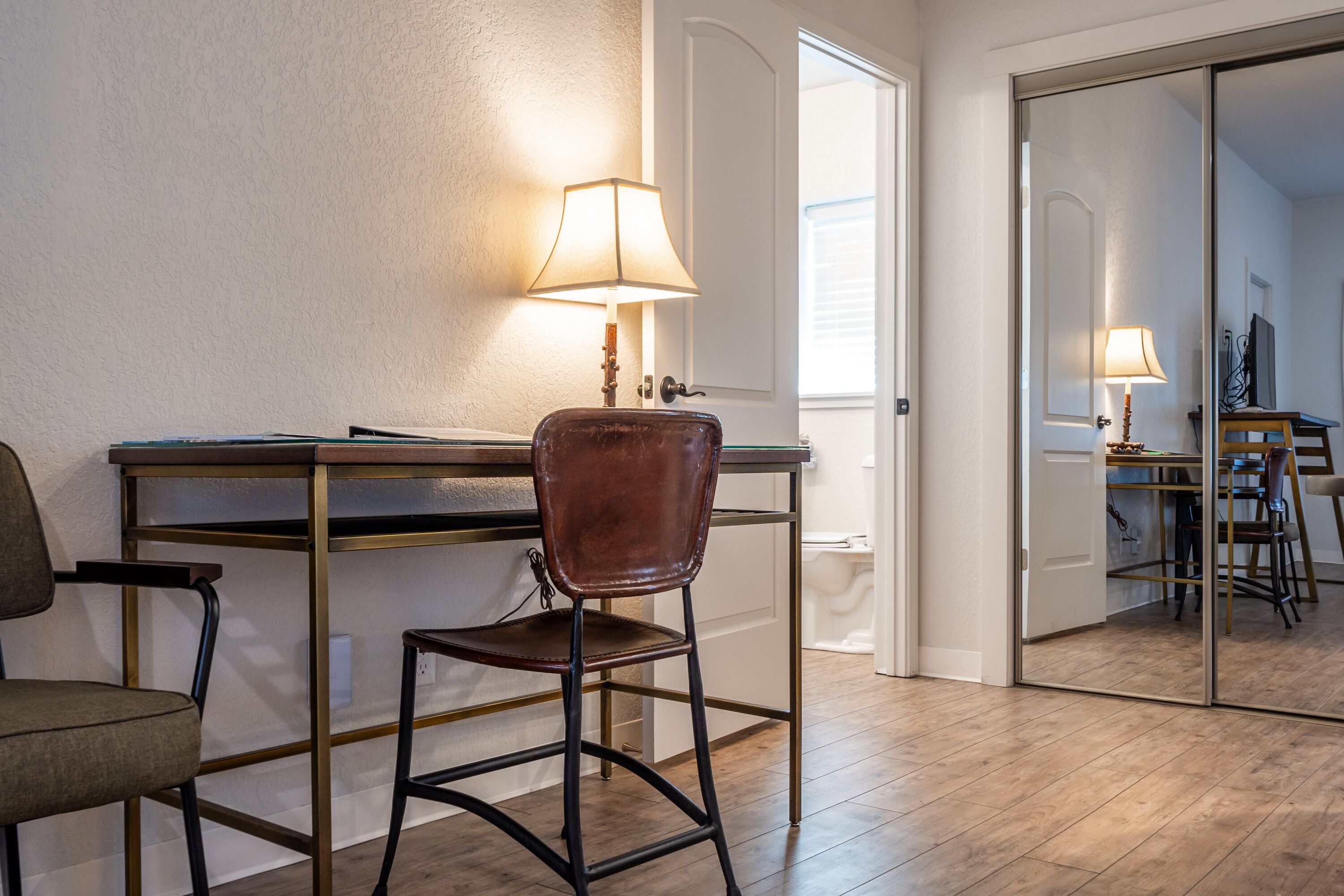 Een kamer met een bureau, een stoel, een lamp en een spiegel.