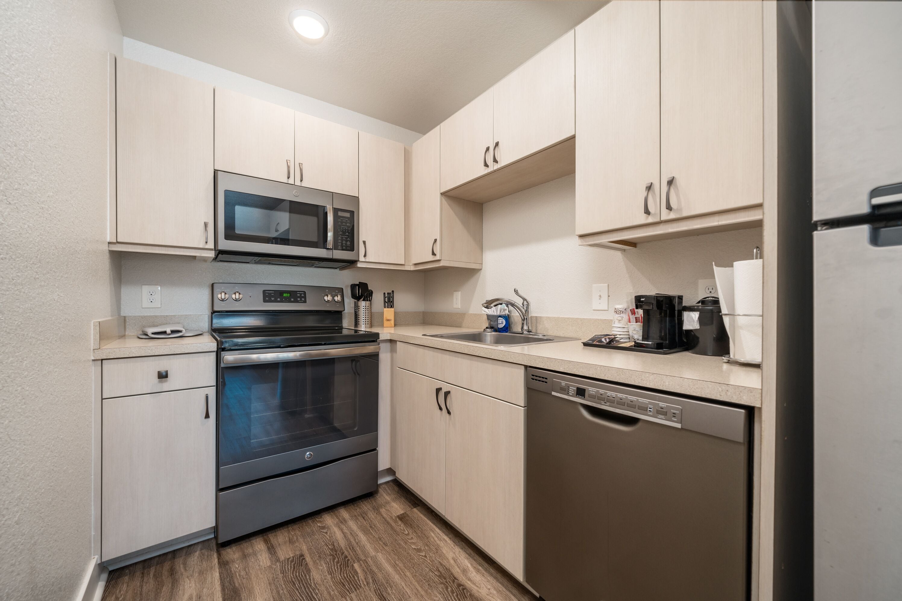 A modern kitchen with stainless steel appliances, light wood cabinets, and a dishwasher.
