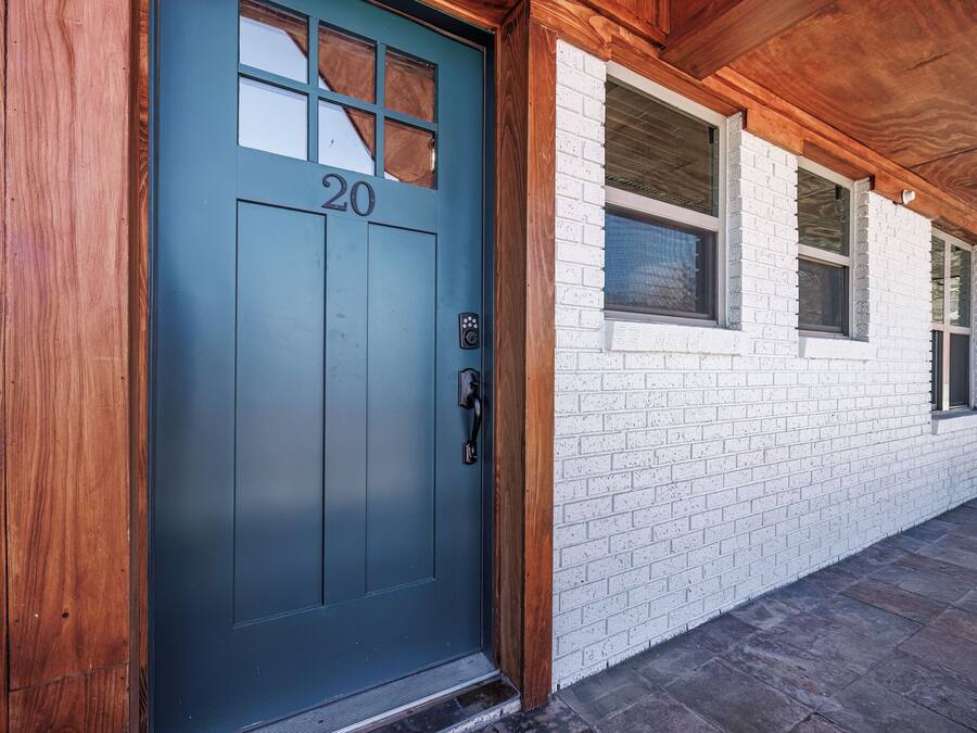 A blue door with the number 20, a wooden door frame, and a white brick wall with windows.