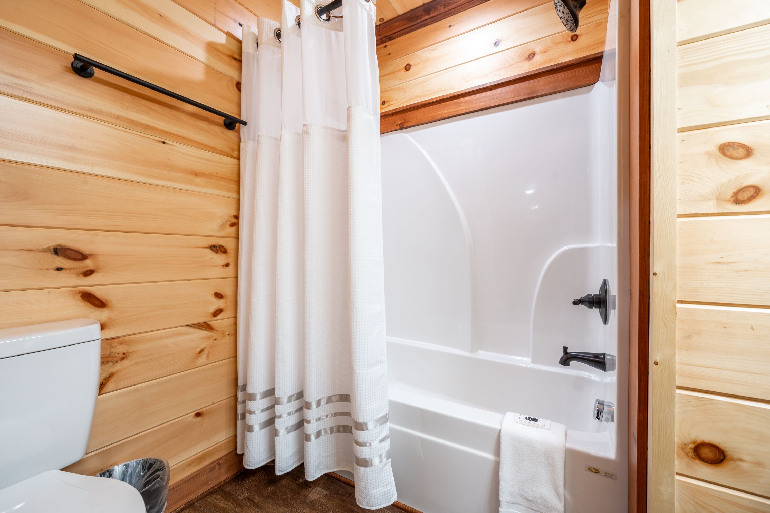Et badeværelse med træpaneler, et hvidt badekar, en brusekabine og et toilet.