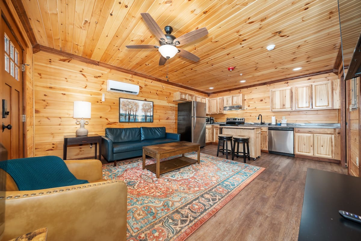 A wooden cabin interior with a living room, kitchen, and dining area.