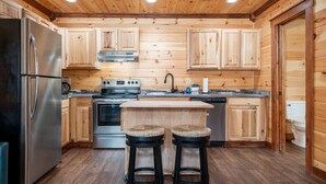 A wooden-paneled kitchen with a stainless steel refrigerator, a stove, and two stools. - Best  Court (Hot Springs)
