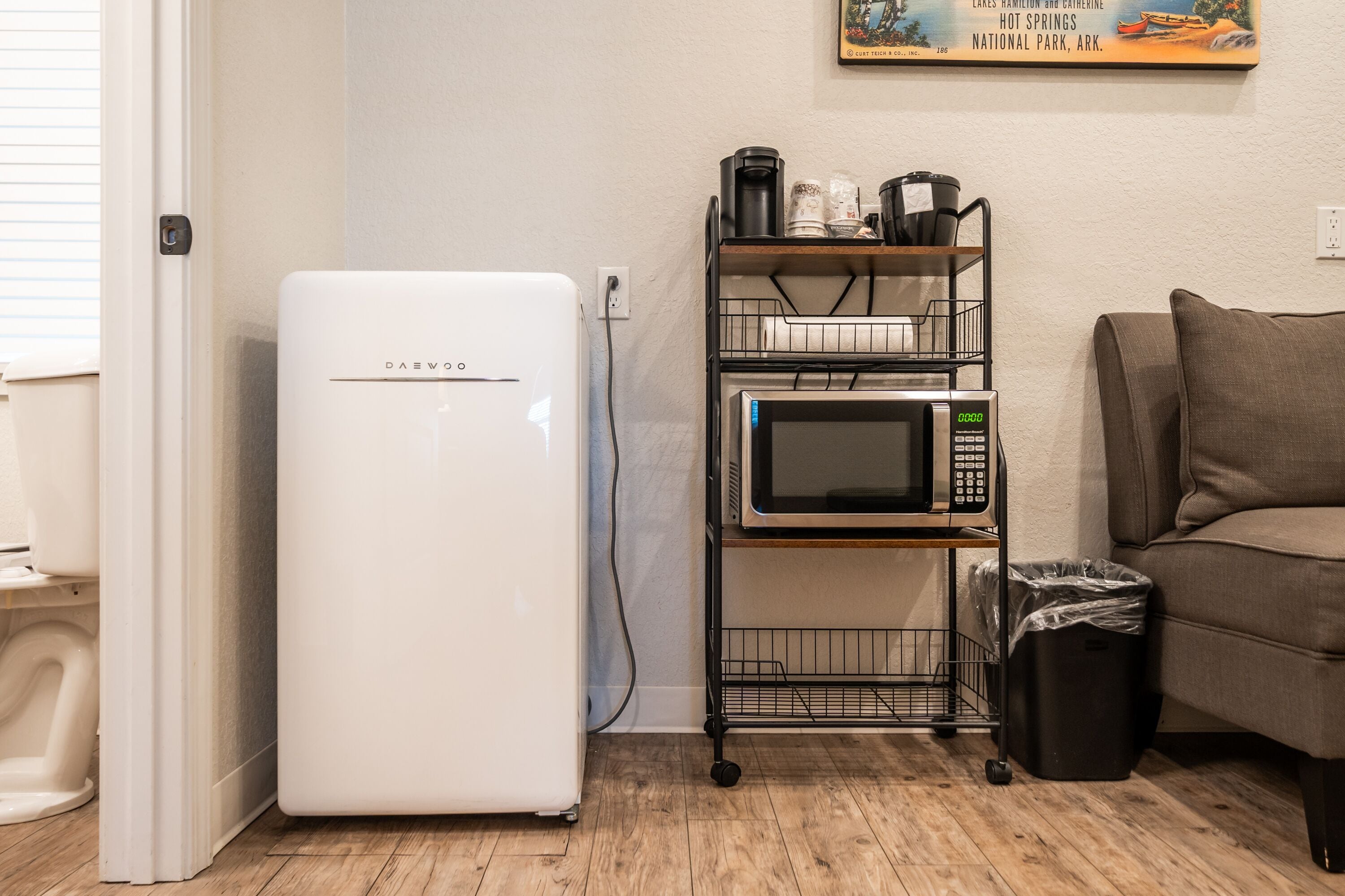A compact kitchenette with a white refrigerator, a microwave, and a coffee maker on a metal cart.