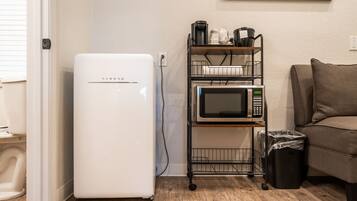 A compact kitchenette with a white refrigerator, a microwave, and a coffee maker on a metal cart.
