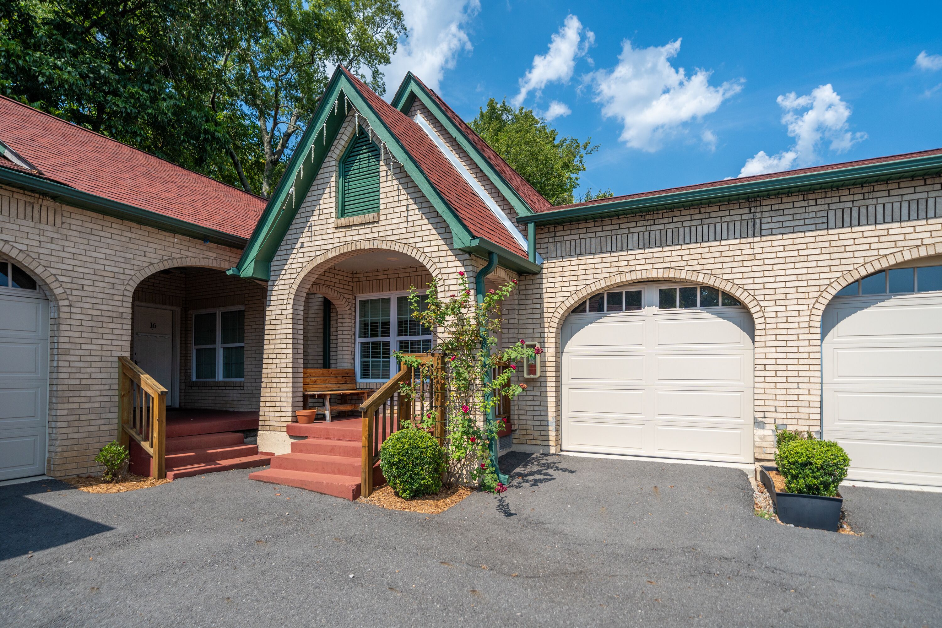 A two-story house with a brick facade, a red roof, and two garage doors.