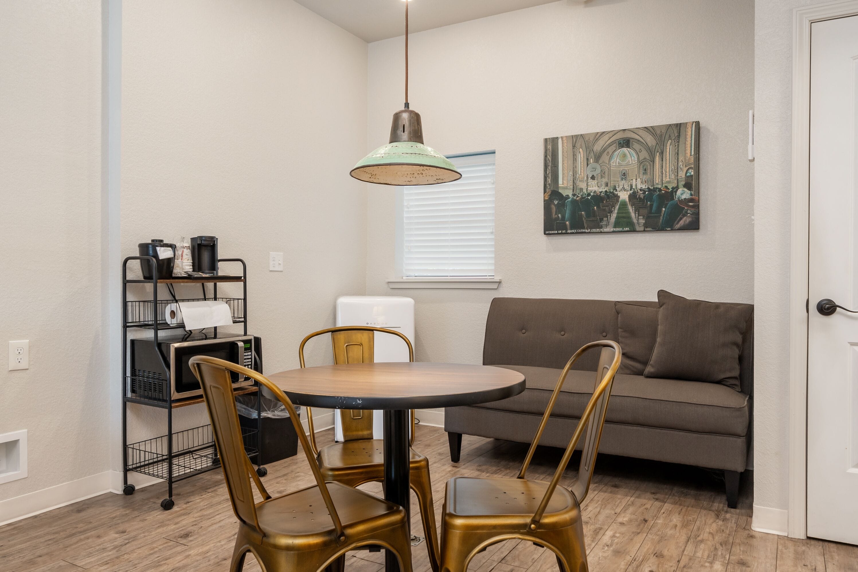 A compact living space with a dining table, four chairs, a sofa, a kitchenette, and a painting on the wall.