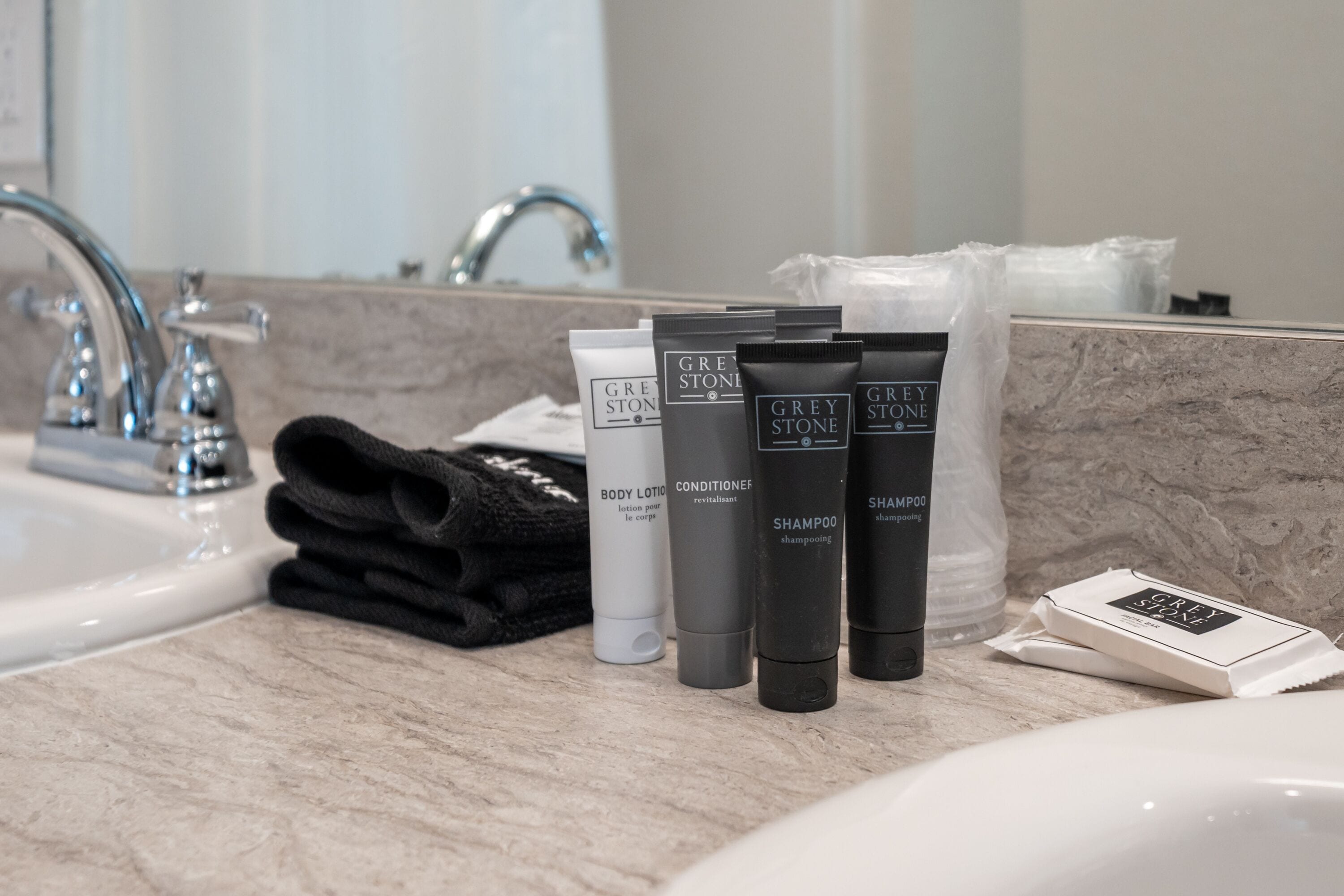 A bathroom counter with Grey Stone body lotion, conditioner, and shampoo, along with a towel and a soap bar.