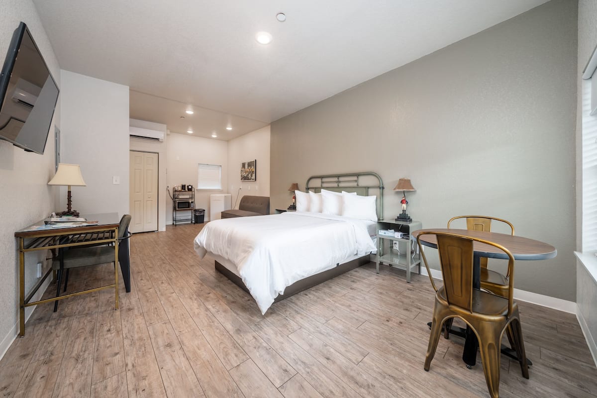 A bedroom with a bed, desk, chair, and a dining table with chairs.