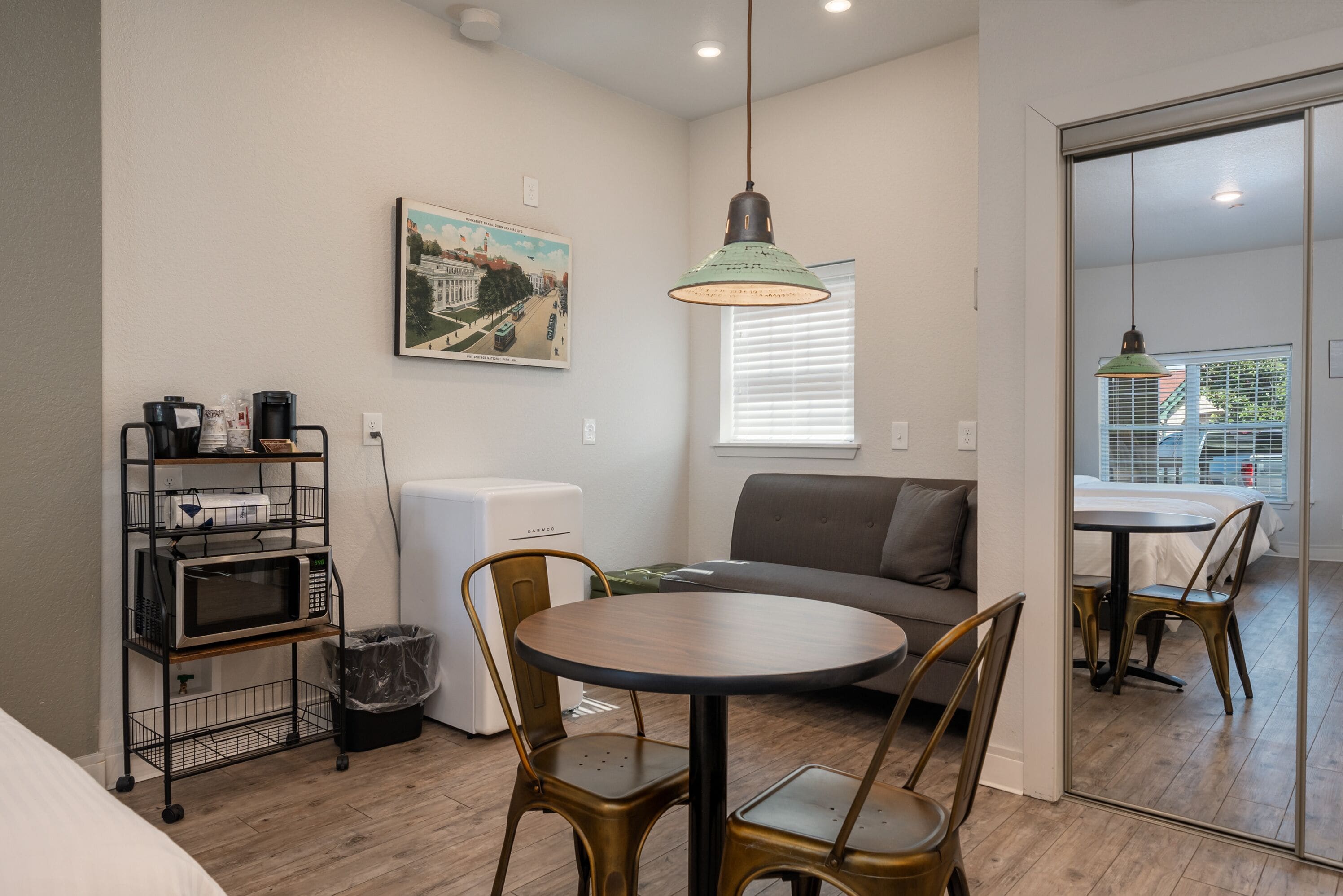 A compact living space with a kitchenette, a dining area with a round table and chairs, a sofa, and a large mirror reflecting the room.