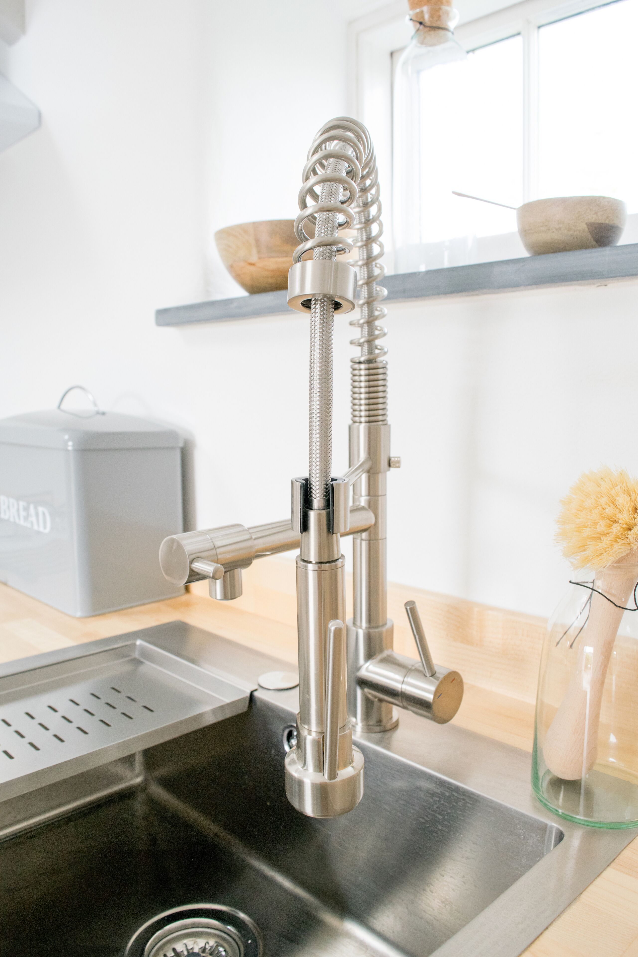 A modern kitchen with a stainless steel sink, a bread box, and a window above the counter.