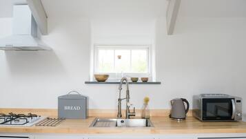 Una cocina moderna con un lavamanos de acero inoxidable, un panera, un hervidor y un microondas.