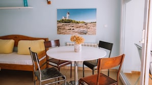 Une pièce confortable avec un lit, une table ronde entourée de chaises, un tableau représentant un phare et une fenêtre donnant sur la mer.