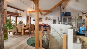 Een ruime woonkamer met een houten trap, een eethoek met rieten meubels, en een keuken met moderne apparatuur.
