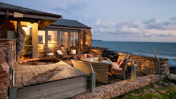 Een stenen huis met een hottub en terras aan de zee.