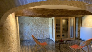 A rustic stone-walled room with wooden flooring, two wooden chairs, a small table, and a glass door leading to a bathroom. - AN AIR OF DETENTE **** (4 ears and 4 stars) (Faudoas)