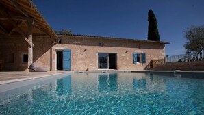 A swimming pool with a clear blue water surface, a brick building with blue shutters, and a tall tree in the background. - AN AIR OF DETENTE **** (4 ears and 4 stars) (Faudoas)