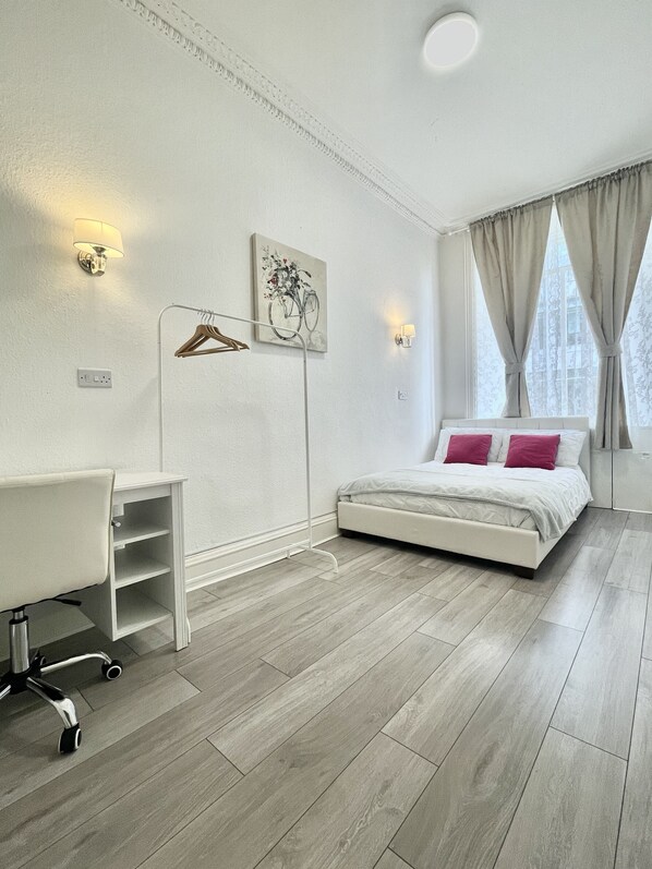 Un dormitorio moderno con cama, escritorio y silla, un cuadro en la pared y una ventana con cortinas.