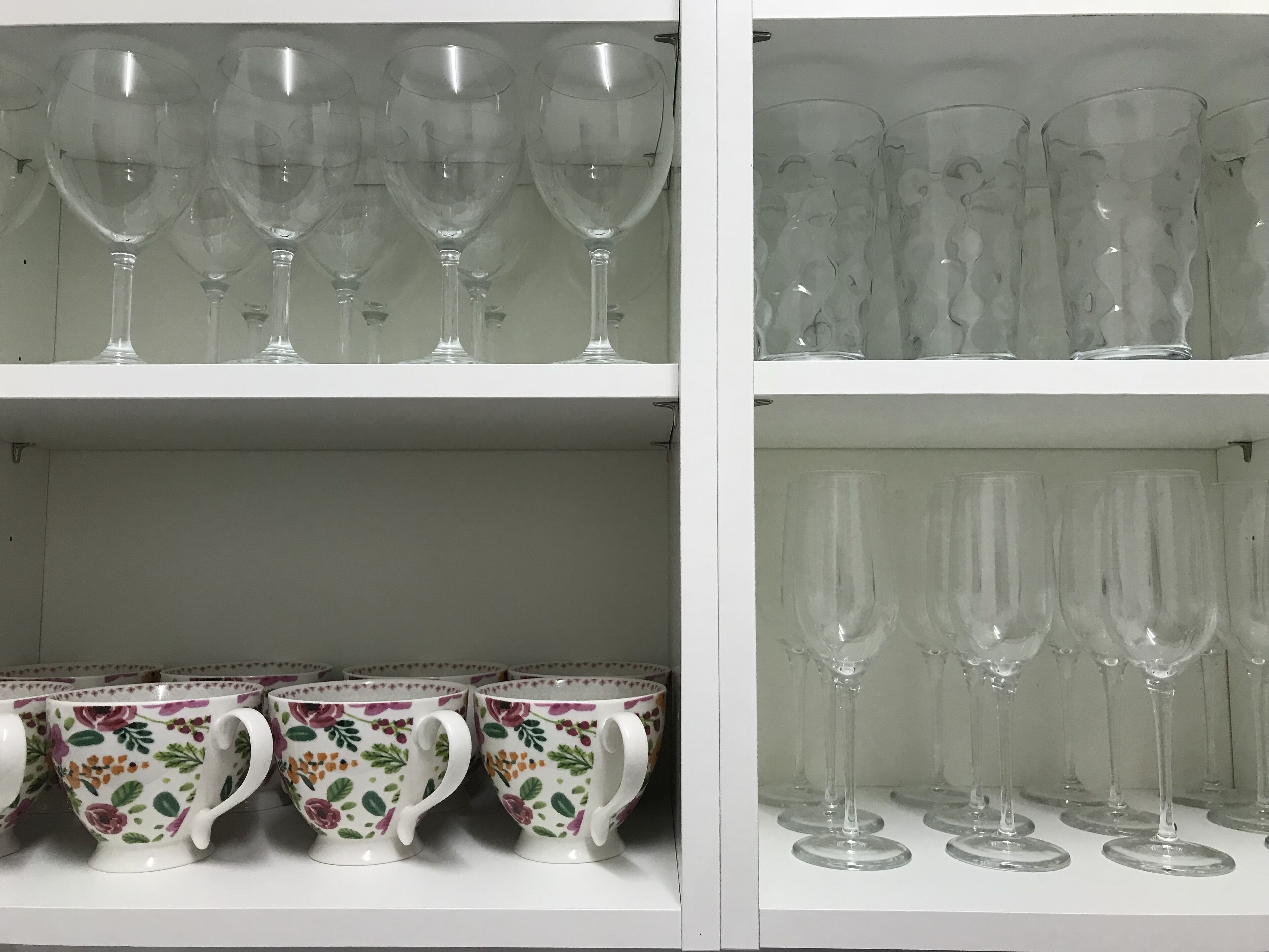 A shelf with clear glass wine glasses and floral-patterned cups.