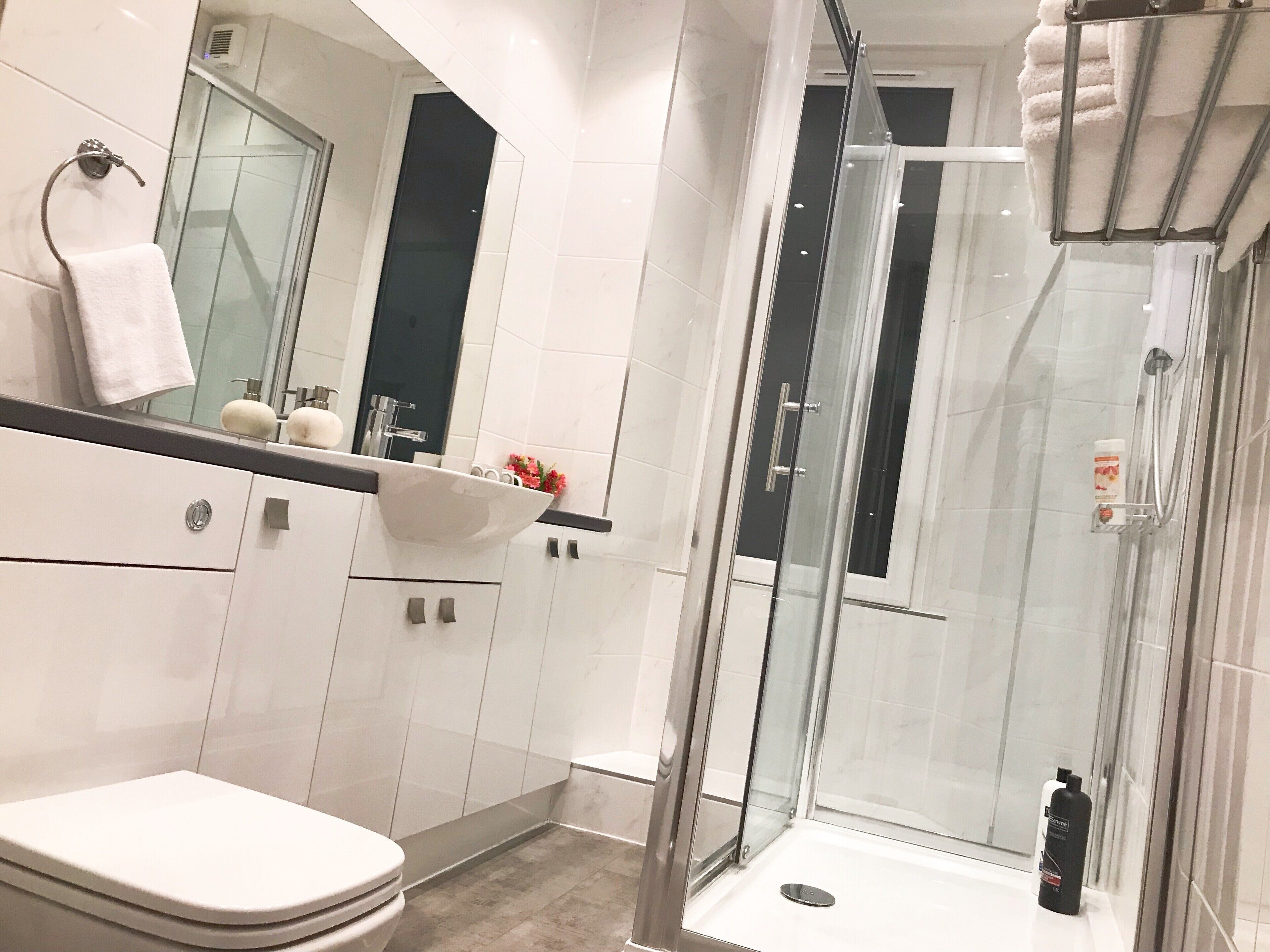 Une salle de bain moderne avec une douche à parois de verre, un lavabo blanc doté d’un plan de toilette en marbre et des toilettes.