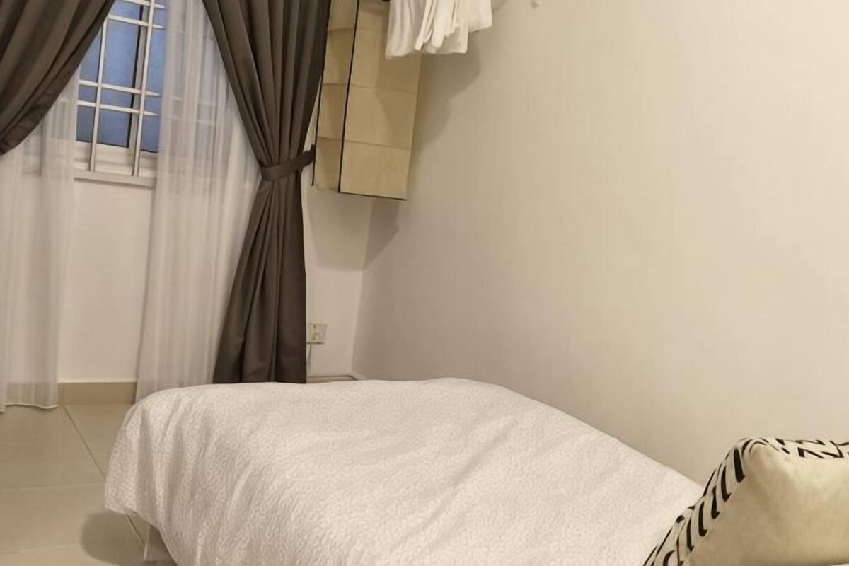 Une chambre à coucher avec un lit, une fenêtre avec des rideaux, un meuble fixé au mur et un mur uni.