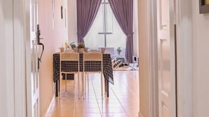 Um corredor leva a uma sala de jantar com mesa e cadeiras, um ventilador de teto e uma janela com cortinas roxas.