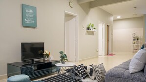 Uma sala de estar moderna com uma televisão de tela plana, uma mesa de centro e um sofá. Há um relógio na parede e uma planta na prateleira.